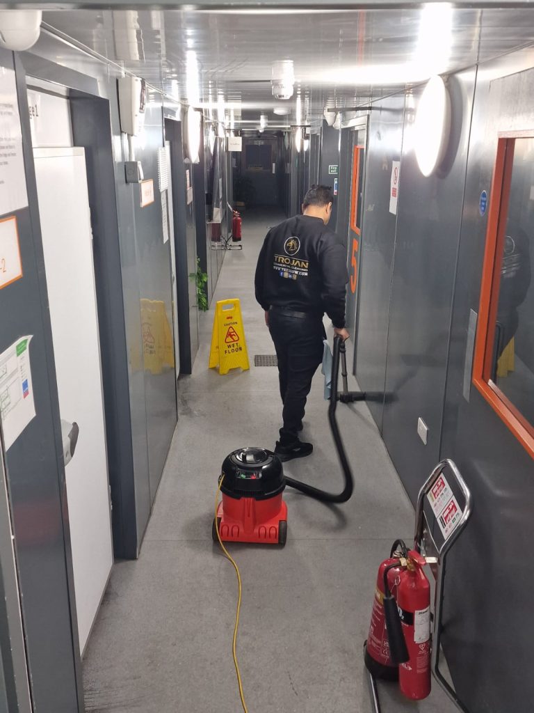 A Trojan FM staff member vaccuming a kitchen hallway floor during a commercial kitchen clean.