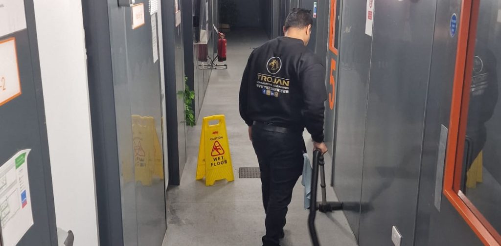 A Trojan FM staff member vaccuming a kitchen hallway floor during a commercial kitchen clean.
